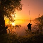 Silhouette of fisherman with fishing rod on the lake at sunset